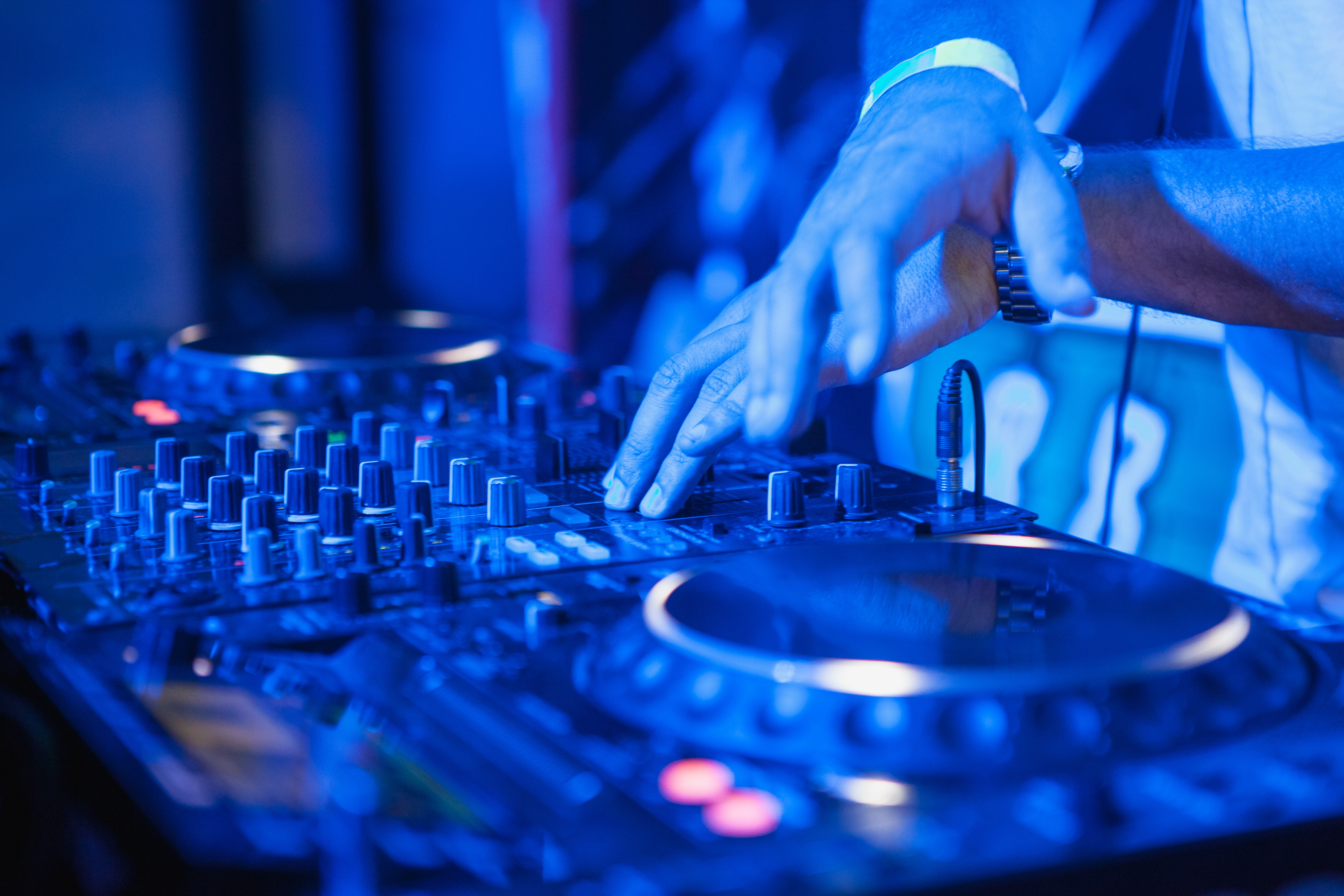 DJ playing music at mixer on colorful blurred background. The hands close up
